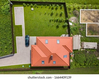 Aerial Top View Of House Shingle Roof With Attic Windows And Black Car On Paved Yard With Green Grass Lawn.