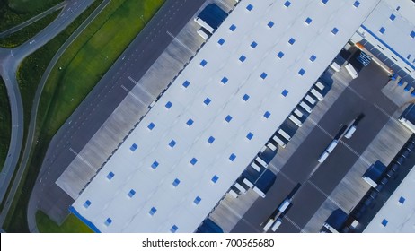 Aerial Top View Of Industrial Storage Building Area With Solar Panels On The Roof And Many Trucks Unloading Merchandise.