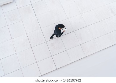 Aerial Top View Of Millennial Hipster Guy Using Modern Digital Tablet For Online Communication Via Application, Male Generation Walking At Urban Setting With Advertising Area Using Public Internet