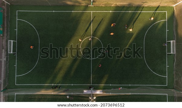 Aerial top view of mini football green field with\
artificial grass made during the soccer match of amateur teams at\
summer day