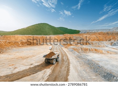 Aerial top view Mining dump truck transporting golden ore on curved haul road in open pit.