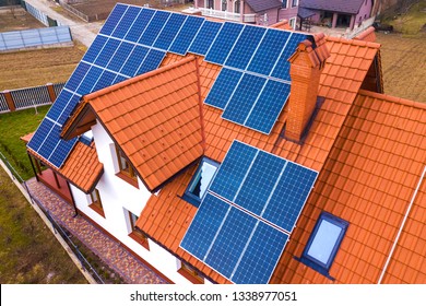 Aerial Top View Of New Modern Residential House Cottage With Blue Shiny Solar Photo Voltaic Panels System On Roof. Renewable Ecological Green Energy Production Concept.