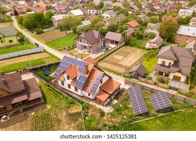 Aerial Top View Of New Modern Residential House Cottage With Blue Shiny Solar Photo Voltaic Panels System On Roof. Renewable Ecological Green Energy Production Concept.