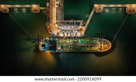 Aerial top view oil tanker ship at terminal industrial port at night for transfer crude oil to oil refinery, Business import export oil and gas petrochemical.