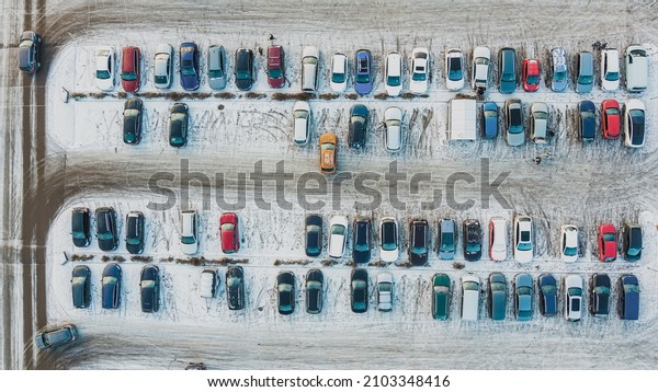 Aerial top view parked snow\
covered cars. Many snowy cars on the parking at the winter\
snowfall.