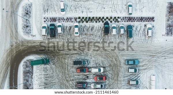 Aerial top view parked snow\
covered cars. Many snowy cars on the parking at the winter\
snowfall.