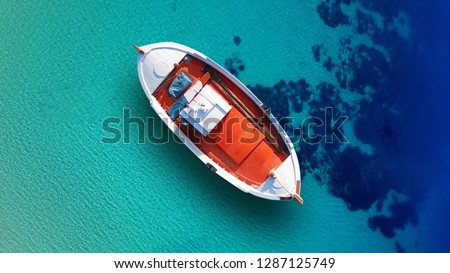 Aerial top view photo of red traditional wooden fishing boat anchored in Aegean island destination port with turquoise sea