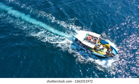 Aerial top view photo of traditional fishing boat cruising in Aegean island destination  port with deep blue sea