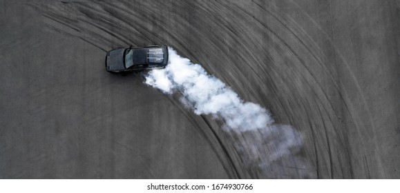 Aerial top view professional driver drifting black car on asphalt road track, Automobile and automotive race car drift on abstract asphalt road tire skid mark with lot of smoke, View from above.
