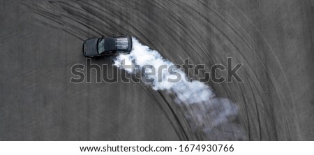 Aerial top view professional driver drifting black car on asphalt road track, Automobile and automotive race car drift on abstract asphalt road tire skid mark with lot of smoke, View from above.