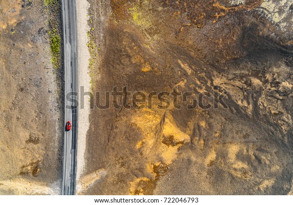 Aerial top view of red car driving on Iceland\
road trip travel adventure. Drone helicopter shot from above of\
volcanic desert landscape. Highway crossing through volcano\
mountains, nature\
background.