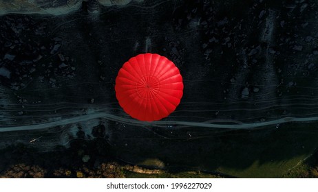 Aerial top view of a red hot air balloon floating over a mountain slope, a narrow path, and a green meadow. Shot. Concept of travelling and adventure.
