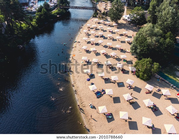 Aerial top view of river\
sand beach with lounges and umbrellas. Local travel concept.\
Sustainable lifestyle, reducing carbon footprint. Drone view of\
riverside resort