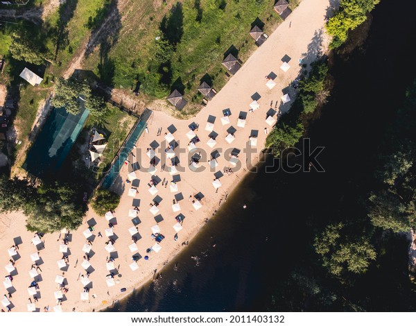 Aerial top view of river\
sand beach with lounges and umbrellas. Local travel concept.\
Sustainable lifestyle, reducing carbon footprint. Drone view of\
riverside resort