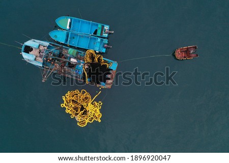 Aerial top view of a small blue colored fishing boat with a fishingnet floating alongside