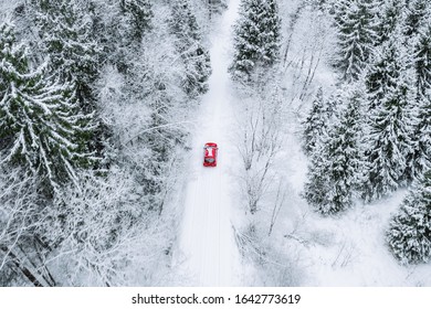 Aerial Top View Of Snow Covered Forest With Winter Road And Red Car. Drone Photography Landscape.