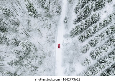 Aerial Top View Of Snow Covered Forest With Winter Road And Red Car. Drone Photography Landscape.