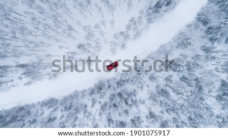 Aerial top view of snow covered forest with winter curving road and red car. Drone photography landscape.
