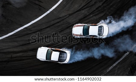 Aerial top view two car drift battle on asphalt race track, Automobile and automotive car view from above, Professional car drifting, Race drift car with white smoke from burning tires on speed track.