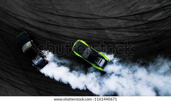 Aerial top view two car drifting battle on asphalt\
street road race track, Two race car drag view from above, Car\
turbo drifting, Race drift car with white smoke from burning tire\
on speed track.