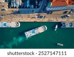 Aerial top view of yachts and boats docked at marina. Ferry docking at pier with tourists walking in port city center