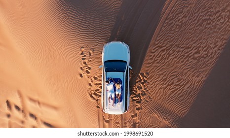 AERIAL. Top view of young couple relaxing on the car's roof at the desert. - Powered by Shutterstock