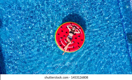 Aerial top of woman wearing a hat sitting in inflatable watermelon in deep cyan calm waters like a pool