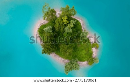 Aerial top-down drone view of a small lush green island surrounded by turquoise water of Lago di Tenno in northern Italy. Captured on a bright summer day, this scenic landscape showcases pristine nature, clear freshwater, and a peaceful remote environment ideal for travel, tourism, and outdoor exploration themes.
