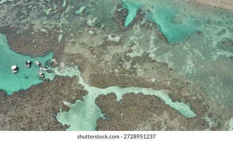 Aerial top-down view of Pontal do Cupe Beach in Porto de Galinhas, Ipojuca, Pernambuco. People swimming in the turquoise water and natural pools formed by coral reefs on beautiful sunny day in Brazil.