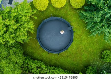 Aerial top-down view of a teenage girl jumping on a trampoline in a backyard. Backyard kids fun. Summer outdoor leisure activities.