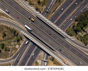 Aerial top-down view of two multilane highways crossing at near-perpendicular angles. Yellow construction truck and white lorry on upper overpass