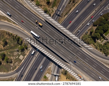 Aerial top-down view of two multilane highways crossing at near-perpendicular angles. Yellow construction truck and white lorry on upper overpass