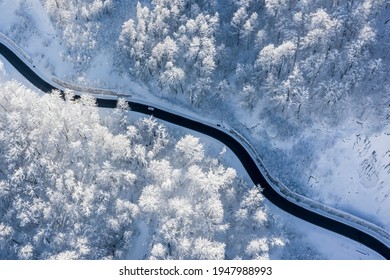 Aerial Top-down Winter Landscape Of Winding Mountain Road In A Snow-covered Forest Lit By A Rising Sun. One Car, No People. High Contrast, Blue Hues