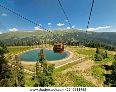 The aerial tramway lifts up with a view of a blue lake in the mountains and a green forest in the background. Arkhyz, Karachay-Cherkessia, Russia