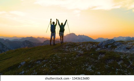 AERIAL: Unrecognizable young hiker couple outstretch arms as they catch the sunset while hiking in the Julian Alps. Picturesque shot of golden sunrise illuminating the excited male and female trekkers - Shutterstock ID 1343613680