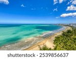 Aerial vantage of Isla Verde Beach in Carolina, Puerto Rico, featuring expansive golden sands, clear turquoise waters, and a backdrop of palm trees and coastal residential buildings under a blue sky.