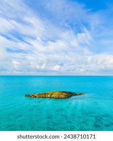 aerial vertical angle of small uninhabited island in pretty blue Caribbean Sea water on sunny day with blue sky and some clouds