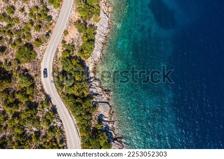 Aerial vertical shot of pickup truck moving by the curved road near sea tranquil waves on coast on Cephalonia Greek island. Transportation, traveling and nature concept.