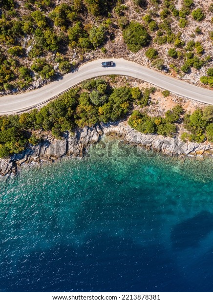 Aerial vertical shot of\
pickup truck moving by the curved road near sea tranquil waves on\
coast on Cephalonia Greek island. Transportation, traveling and\
nature concept.