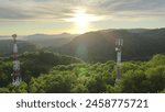 Aerial view of 5G telecom tower antenna for data internet wireless smartphone generation. Drone shoot in the middle of a green forest during an epic sunrise in a mountain landscape