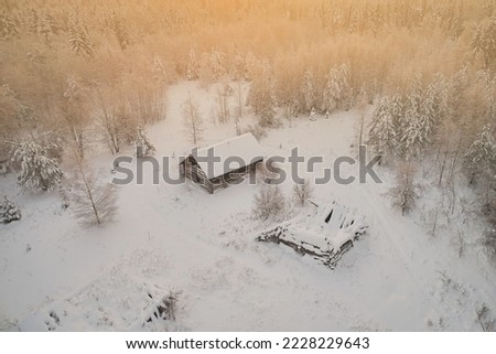 Aerial view of an abandoned village in the forest with destroyed houses against the backdrop of snow and winter landscape. Warm sunset color