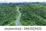 Aerial view from above of country road through the green summer forest in summer Thailand. Top view of the asphalt road and dense green forests.