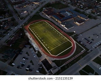 An Aerial View Above A New, Municipal, Small City Football Field Is Seen Illuminated At Night, As A Game Is Being Played.