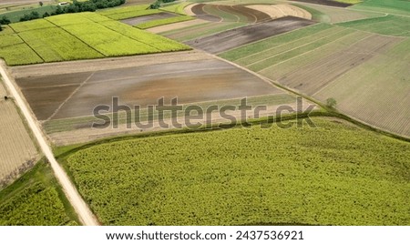 an aerial view of agricultural fields showing various stages of cultivation. There is a mix of planted crops, plowed fields, and possibly fallow land. 