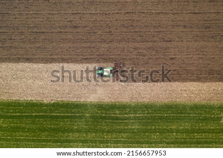 Aerial view of agricultural tractor tilling and harrowing ploughed field, directly above drone pov image of machinery working on farmland