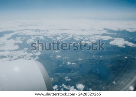 An aerial view from an airplane reveals a sprawling tapestry of land and clouds, a serene scene of Earth's beauty from above. The jet engine peeks into the frame, symbolizing human ingenuity.