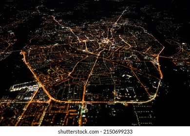 Aerial view from airplane window of buildings and bright illuminated streets in city residential area at night. Dark urban landscape at high altitude - Powered by Shutterstock