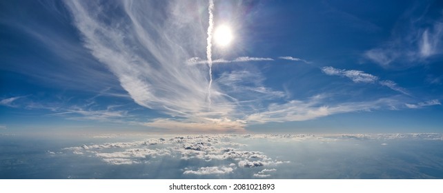 Aerial view from airplane window at high altitude of earth covered with white thin layer of misty haze and distant clouds.