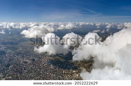 Aerial view from airplane window at high altitude of distant city covered with puffy cumulus clouds forming before rainstorm.