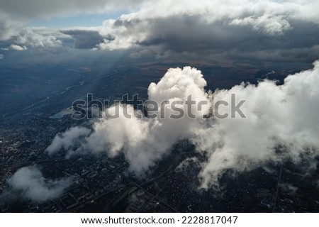Aerial view from airplane window at high altitude of distant city covered with puffy cumulus clouds forming before rainstorm